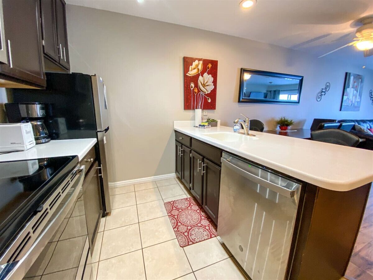 A compact kitchen with a dishwasher, a stove, and a microwave. There is a red patterned rug on the floor.