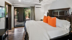 Een hotelkamer met een groot bed, een plafondventilator, een schuifdeur naar buiten en een kleine tafel.