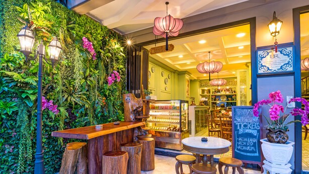 An indoor cafe with a green wall, wooden stools, and a bar area. - U Residence Hotel (Krabi)