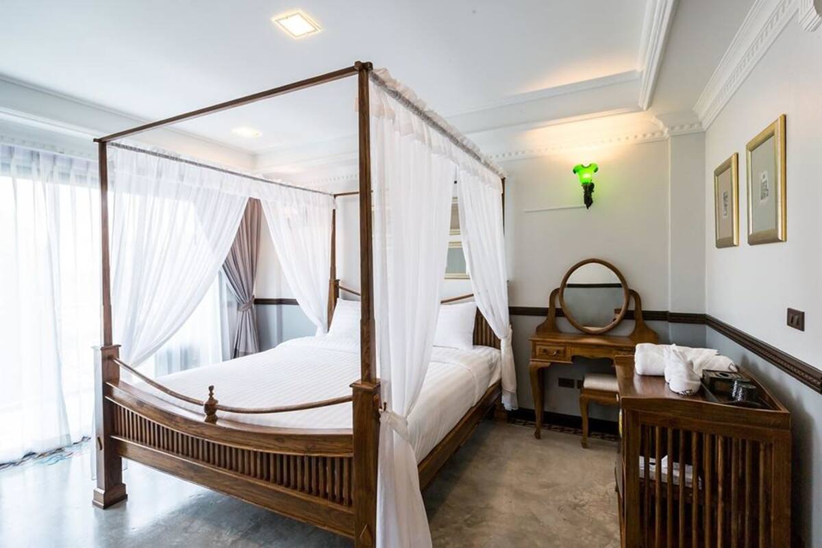 A four-poster bed with a canopy, a wooden desk with a mirror, and a bedside table with a lamp.
