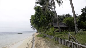 A beach with a wooden fence, palm trees, and a thatched-roof building. - Yama Beachfront House (General Luna)