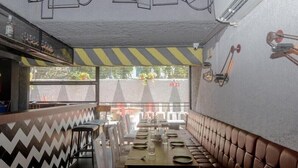 A restaurant with a long wooden table set for dining, cushioned booths along the walls, and a view of the street outside. - Hotel Jayshree (Mumbai)