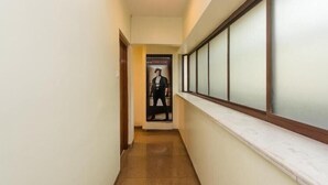 A hallway with a poster on the wall, a window with blinds, and a marble ledge. - Hotel Jayshree (Mumbai)