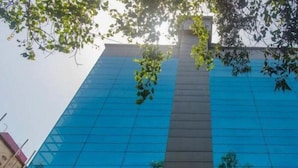A tall building with a reflective glass facade, surrounded by trees. - Hotel Jayshree (Mumbai)