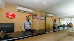A reception area with a glass counter, a computer monitor, and a red OYO logo on the wall. - Hotel Jayshree (Mumbai)