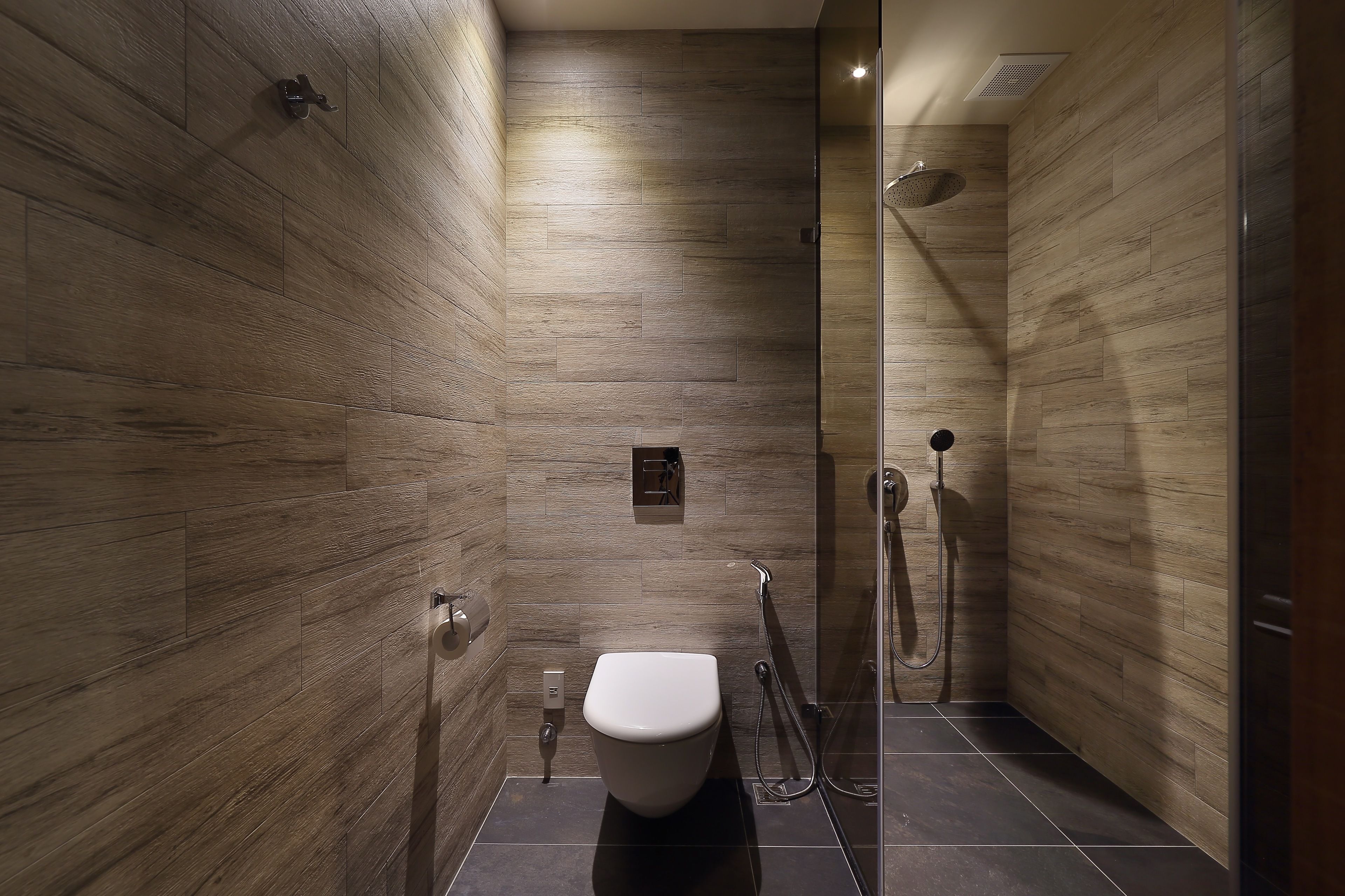 A modern bathroom with a wooden wall design, a toilet, and a glass-enclosed shower area.