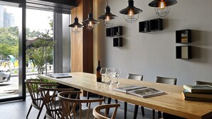 A modern dining area with a long wooden table, several chairs, pendant lights, and a view through large windows. - Blue Sky Bay B&B (Yuchi)
