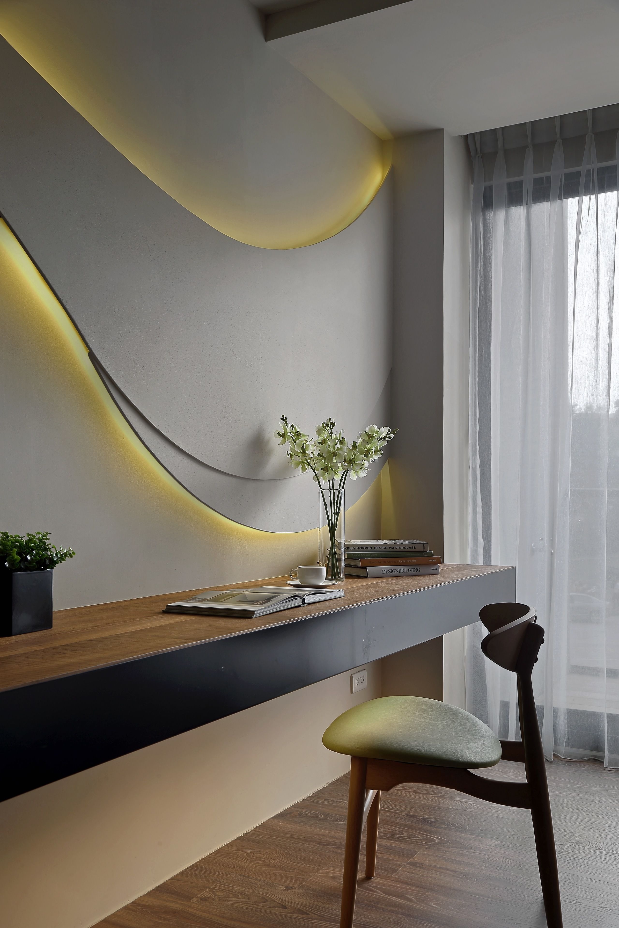 Un interior moderno con una pared curva, un escritorio de madera, una silla y una ventana con cortinas translúcidas.