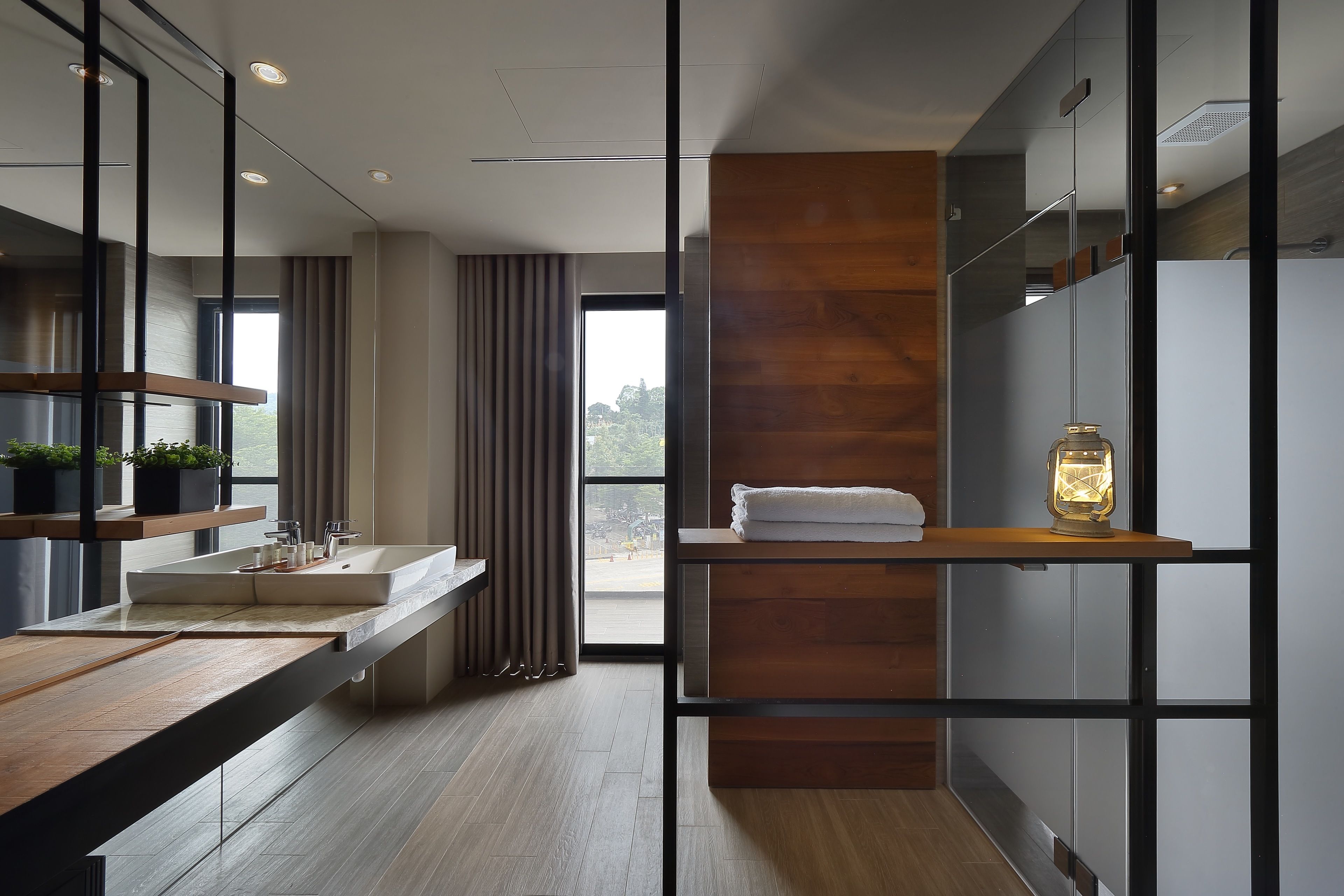 A modern bathroom with a wooden vanity, a large mirror, and a window providing a view of the outdoors.