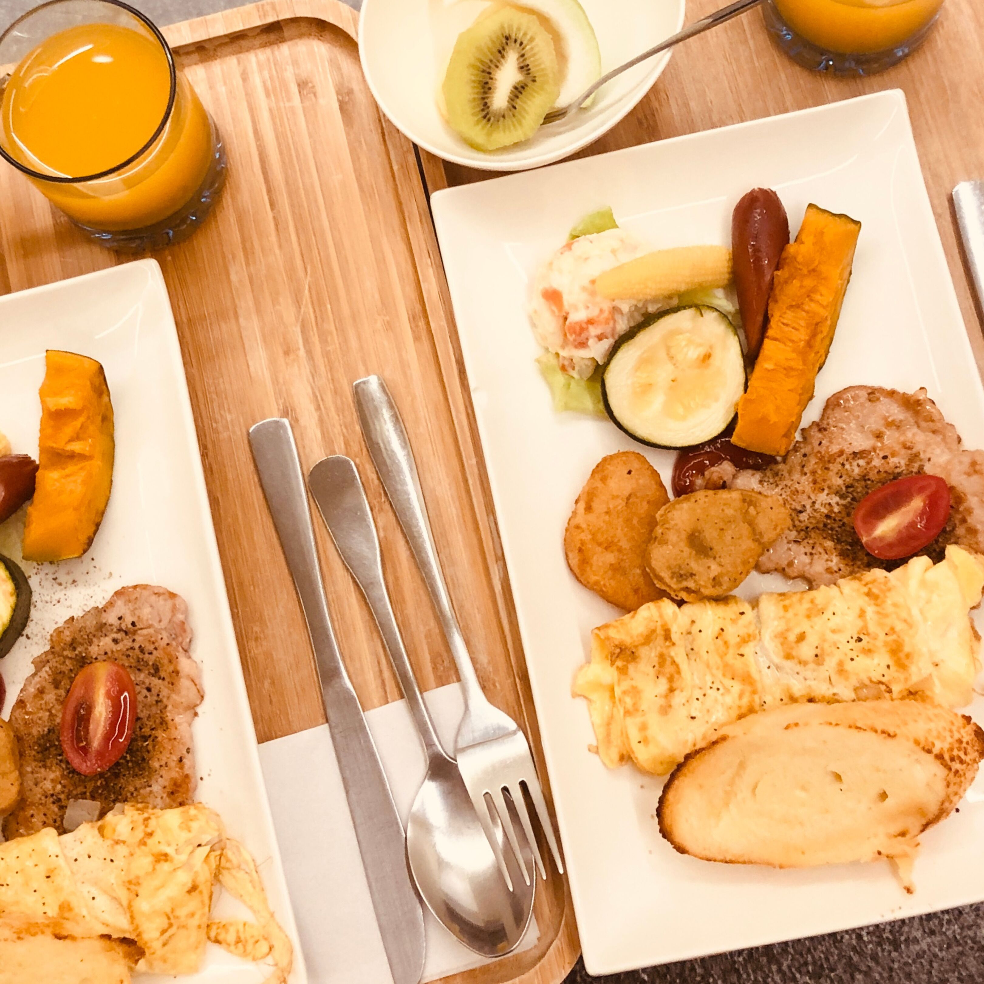 A breakfast tray with plates of food, cutlery, and a glass of orange juice.
