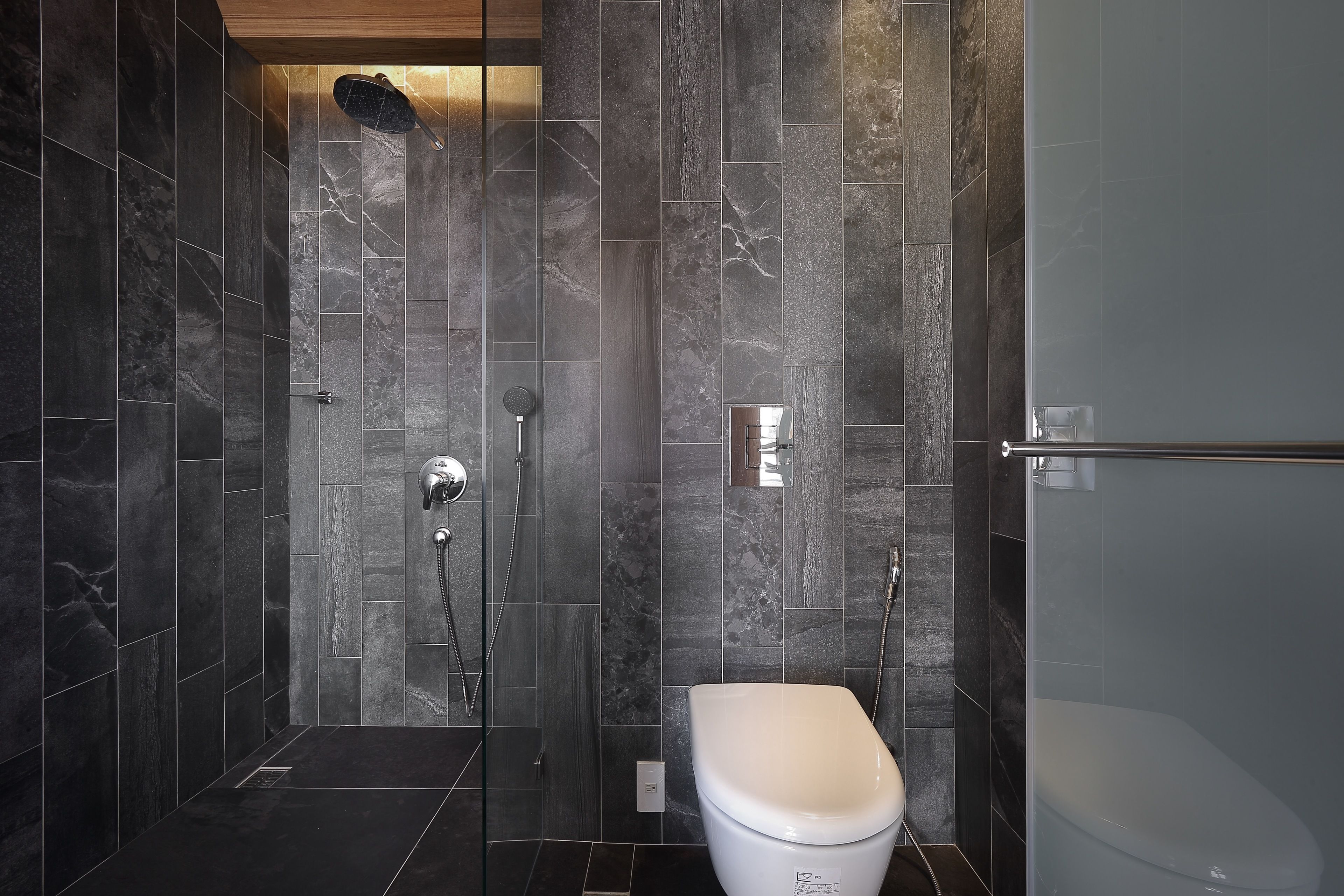 Un baño moderno con baldosas de mármol oscuro, una ducha con cerramiento de vidrio y un inodoro blanco.