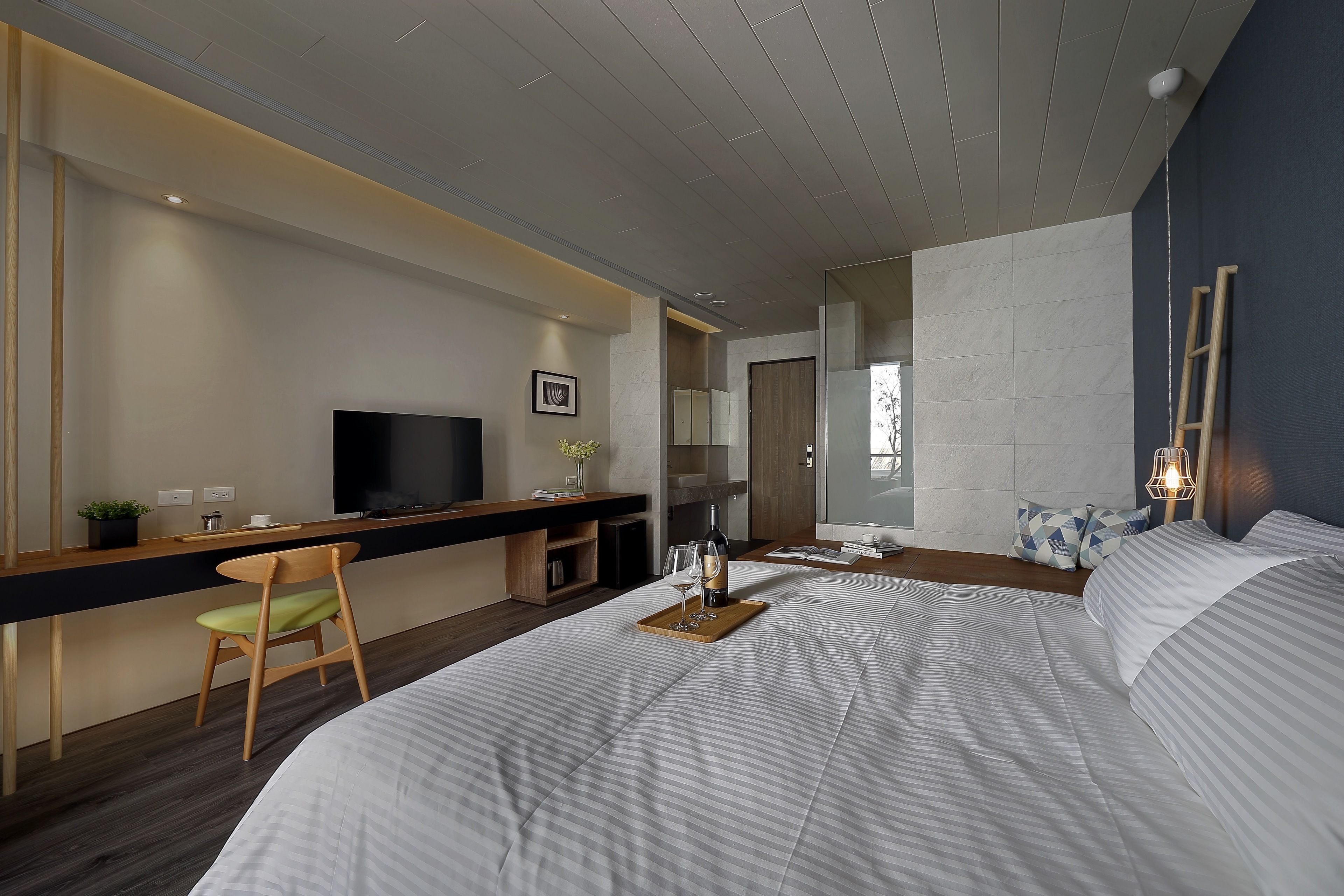 Une chambre d’hôtel moderne dotée d’un grand lit, d’un bureau avec une télévision et d’un coin salon avec un fauteuil.