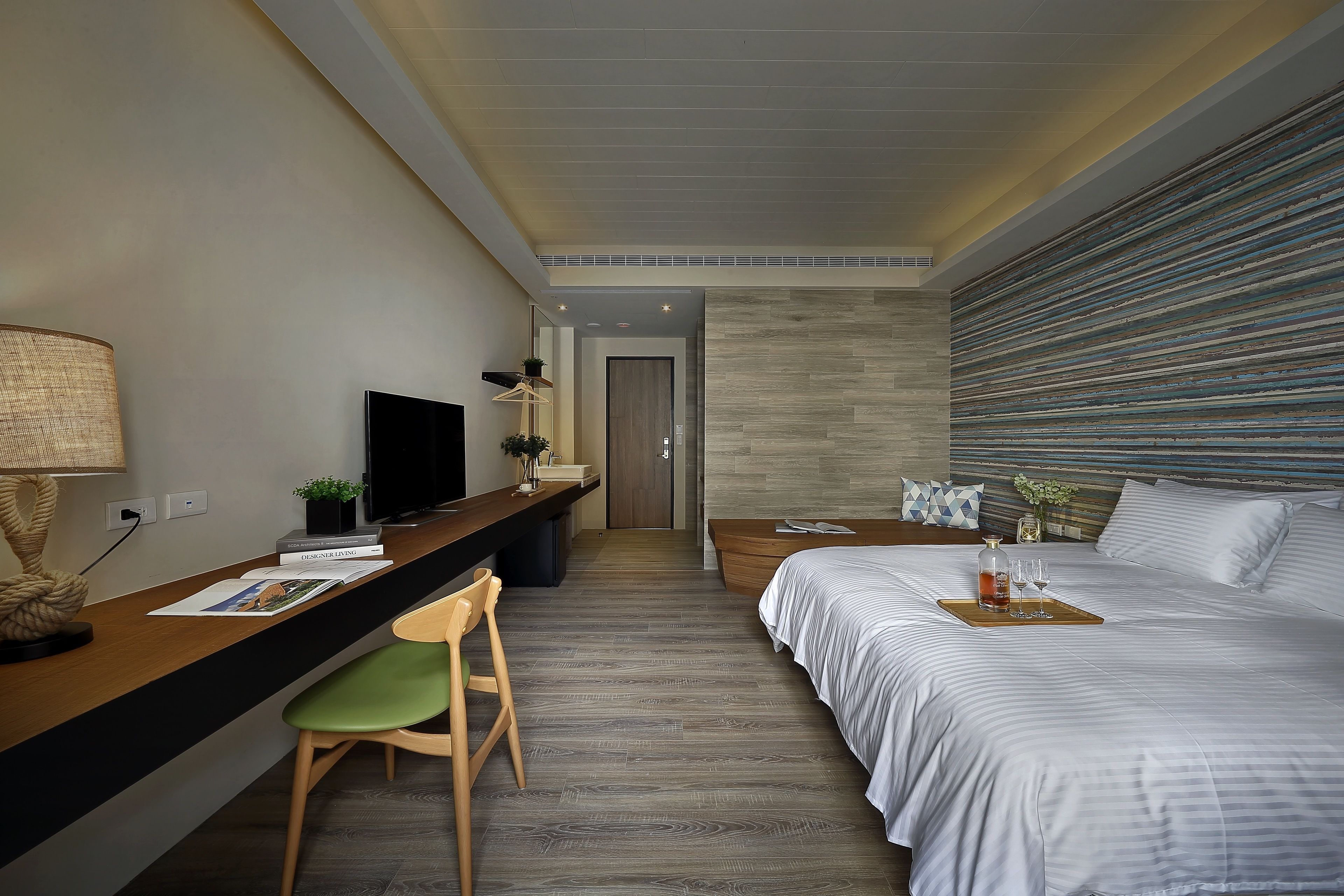 Ein modernes Hotelzimmer mit einem Holztisch, einem bequemen Sessel, einem Bett mit Getränketablett und einem Fernseher.