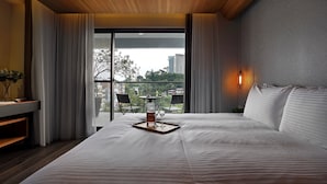 A hotel room with a large bed, a bedside table, a tray with a bottle and glasses, and a balcony with chairs and a table. - Blue Sky Bay B&B (Yuchi)