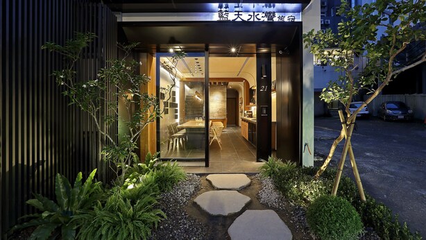 A modern hotel entrance with a glass door, a dining area visible inside, and a well-maintained garden with stepping stones and plants. - Blue Sky Bay B&B (Yuchi)