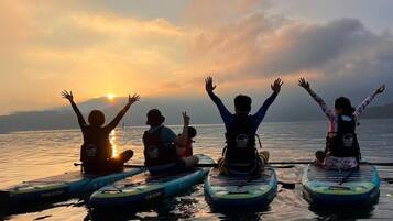 Vier mensen op paddleboards kijken naar een zonsondergang boven kalm water.