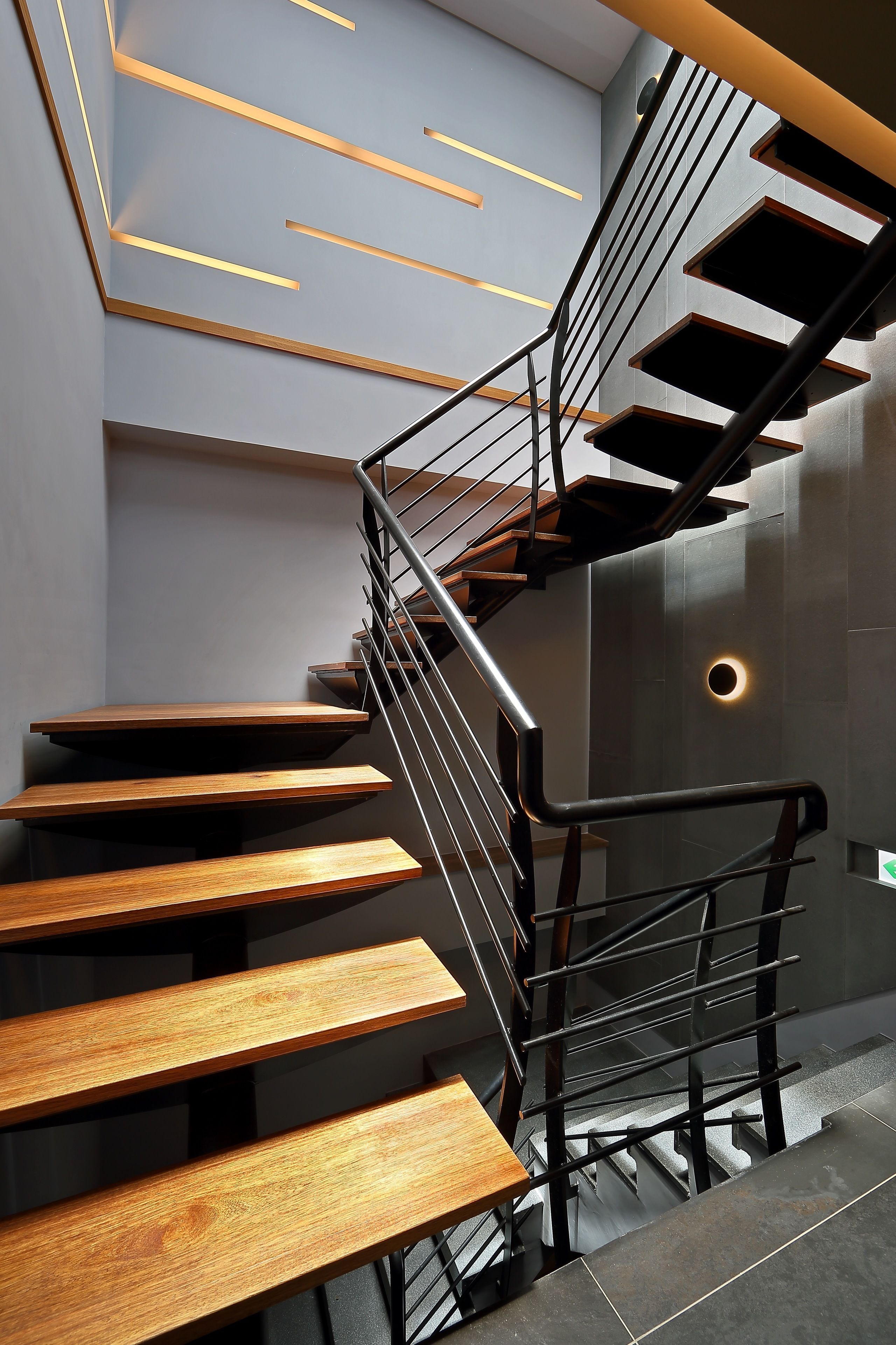 A modern staircase with wooden steps and metal railings, leading to a landing with recessed lighting.