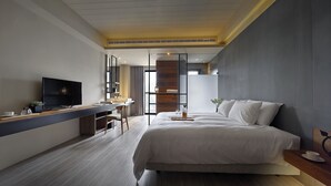 Una habitación de hotel moderna con una cama grande, un escritorio con televisor de pantalla plana y una zona de estar con una silla.