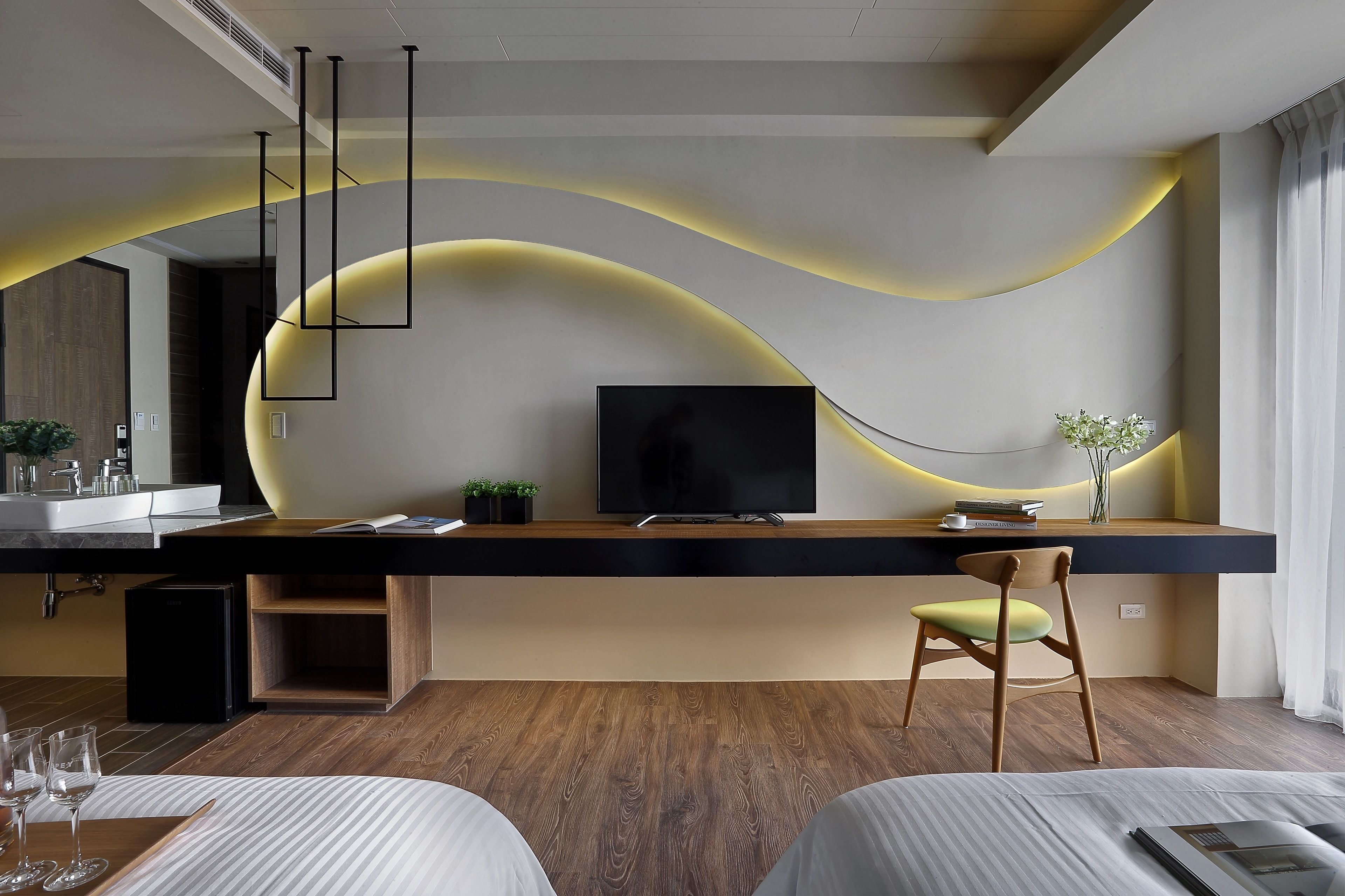Ein modernes Hotelzimmer mit Holzboden, einem großen Flachbildfernseher, einem Essbereich mit Tisch und Stühlen sowie einer integrierten Küche mit Spüle und Arbeitsplatte.