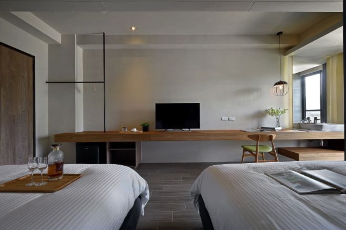A modern hotel room with a long wooden desk, a television, a chair, and two beds.