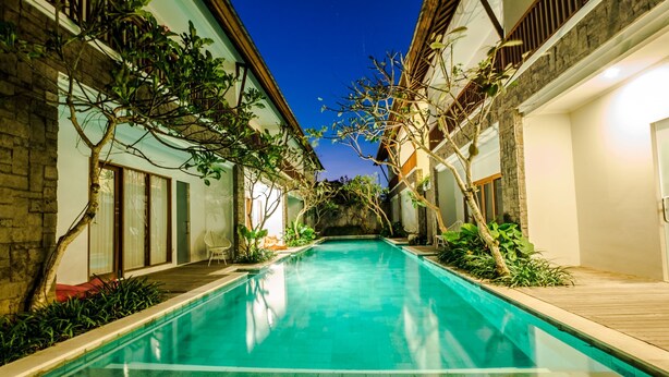 A swimming pool with a clear blue water surface, surrounded by buildings with stone walls and wooden railings.