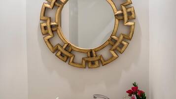 A bathroom with a round mirror, a stone sink, a faucet, and a vase with flowers.