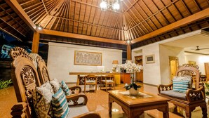 A spacious room with a high wooden ceiling, a dining area with wooden furniture, and a decorative wall piece.