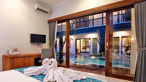 A hotel room with a bed, a desk, a TV, and a view of a pool and balcony.