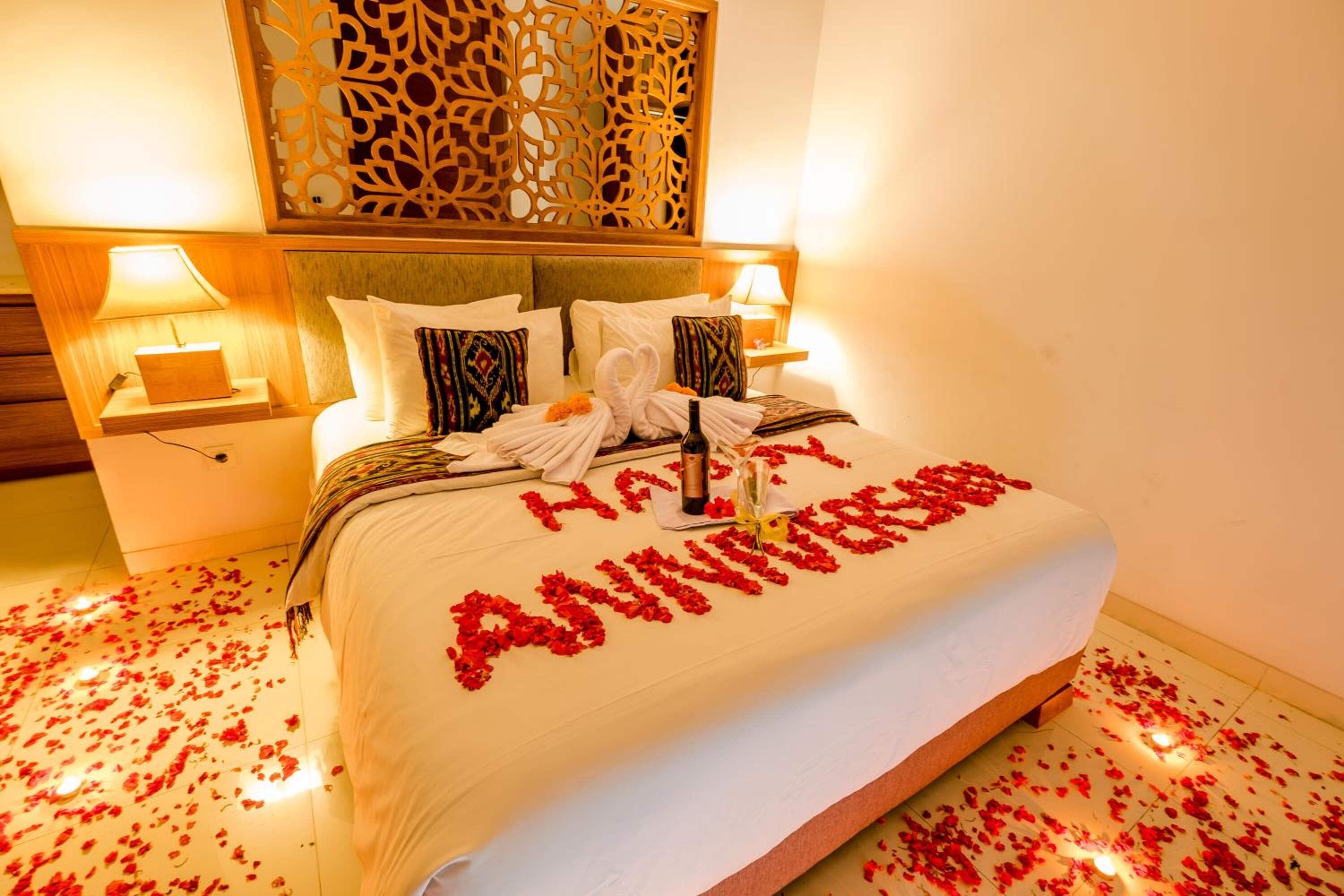 A bed with a white bedspread and a message spelled out with rose petals.