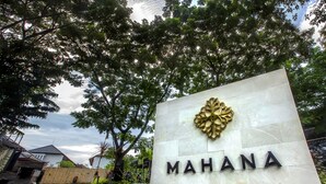 A sign with the word "MAHANA" and a gold emblem, surrounded by trees and a brick pathway.