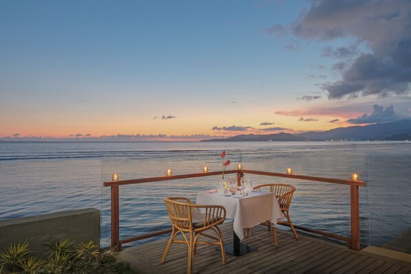 Comedor con una mesa y sillas frente a un cuerpo de agua al atardecer.