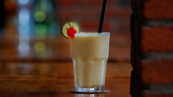 A glass of a creamy beverage with a cherry and lime garnish, a black straw, and a coaster on a wooden surface.