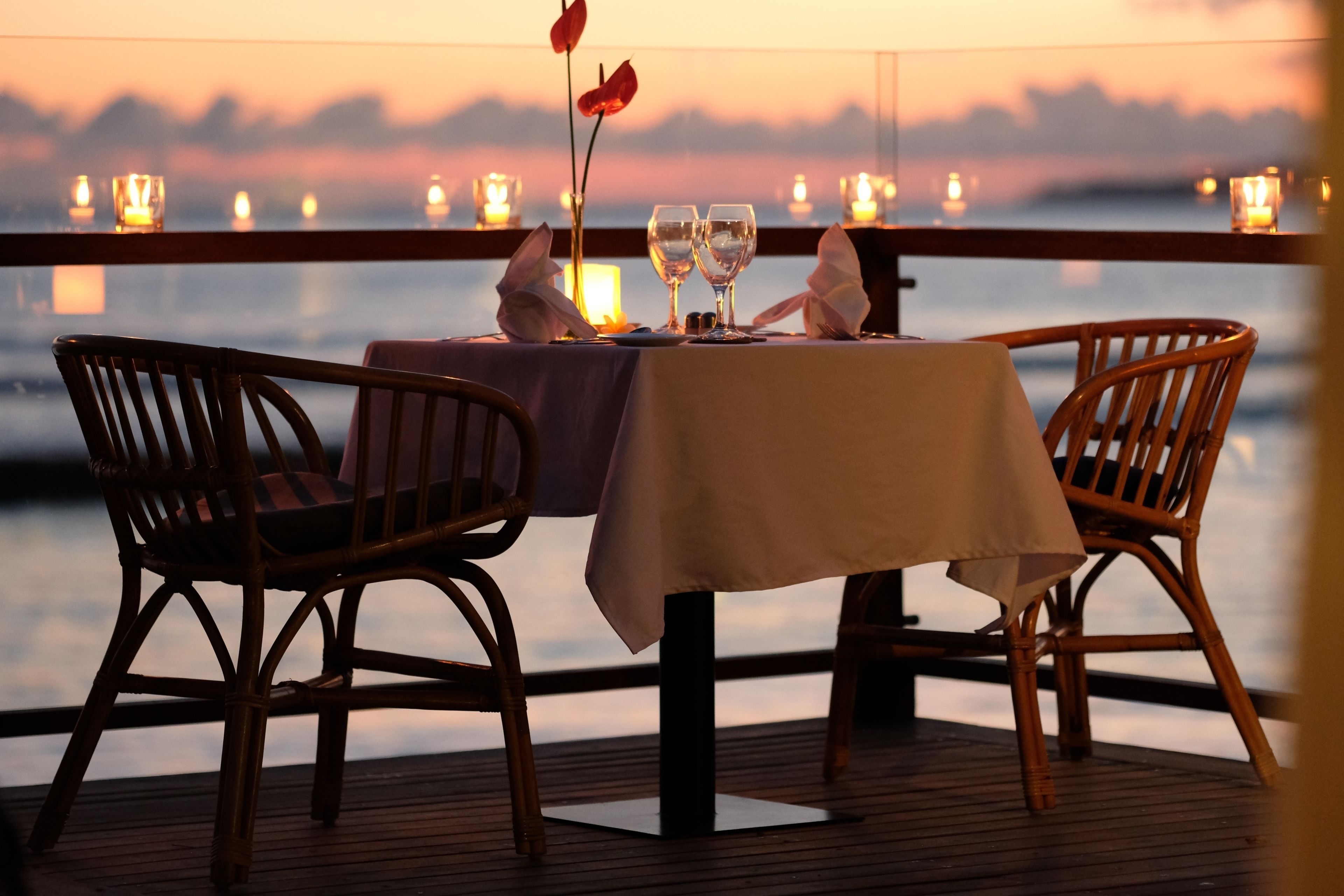 A table set for two with candles, a vase with flowers, and a view of the water at sunset.