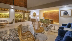 A spacious lobby with wicker furniture, a stone wall, and a wooden ceiling. - Sagara Candidasa by AHM (Karangasem)