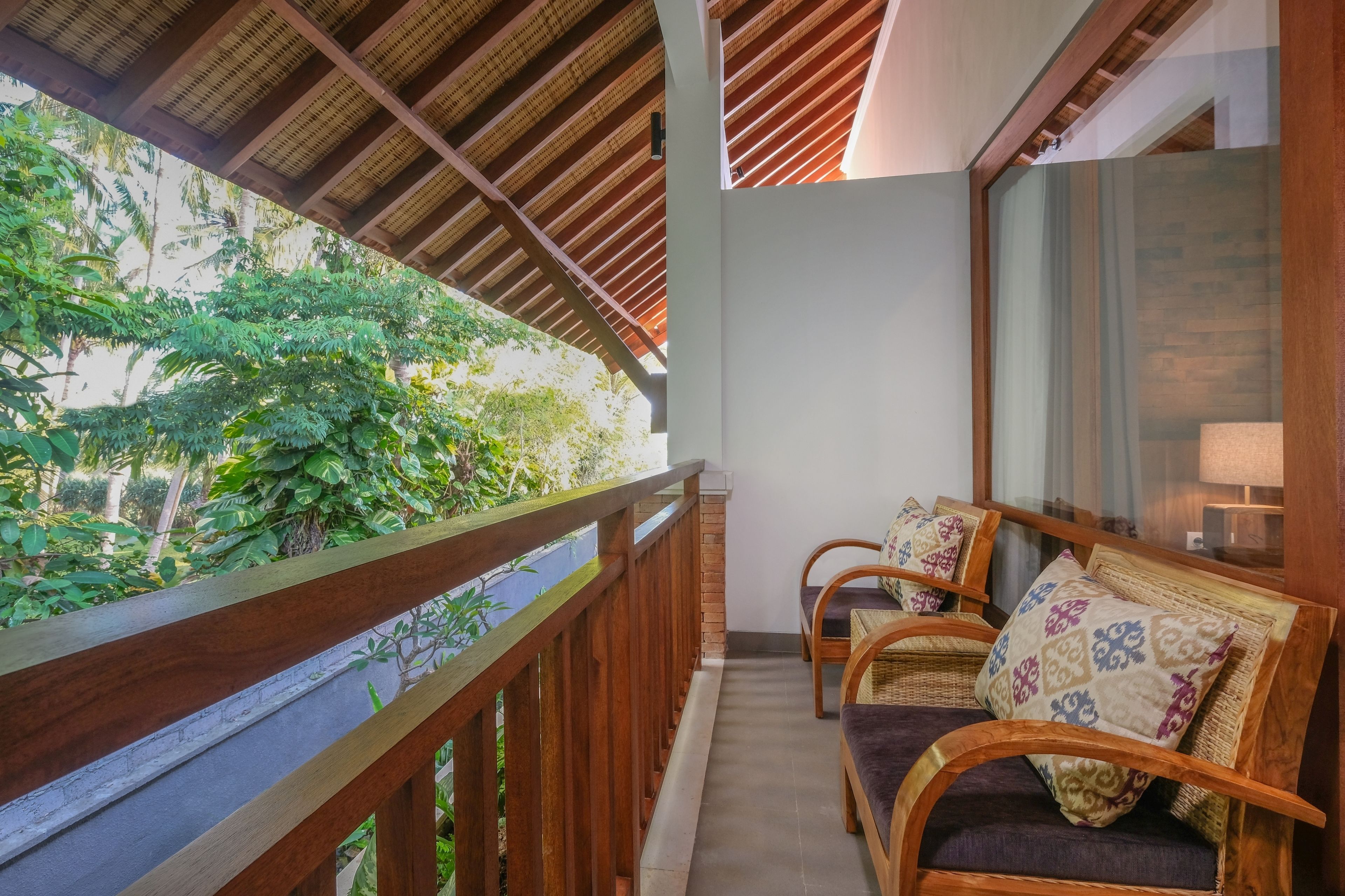 A balcony with wooden railings, wicker chairs with cushions, and a view of lush greenery.