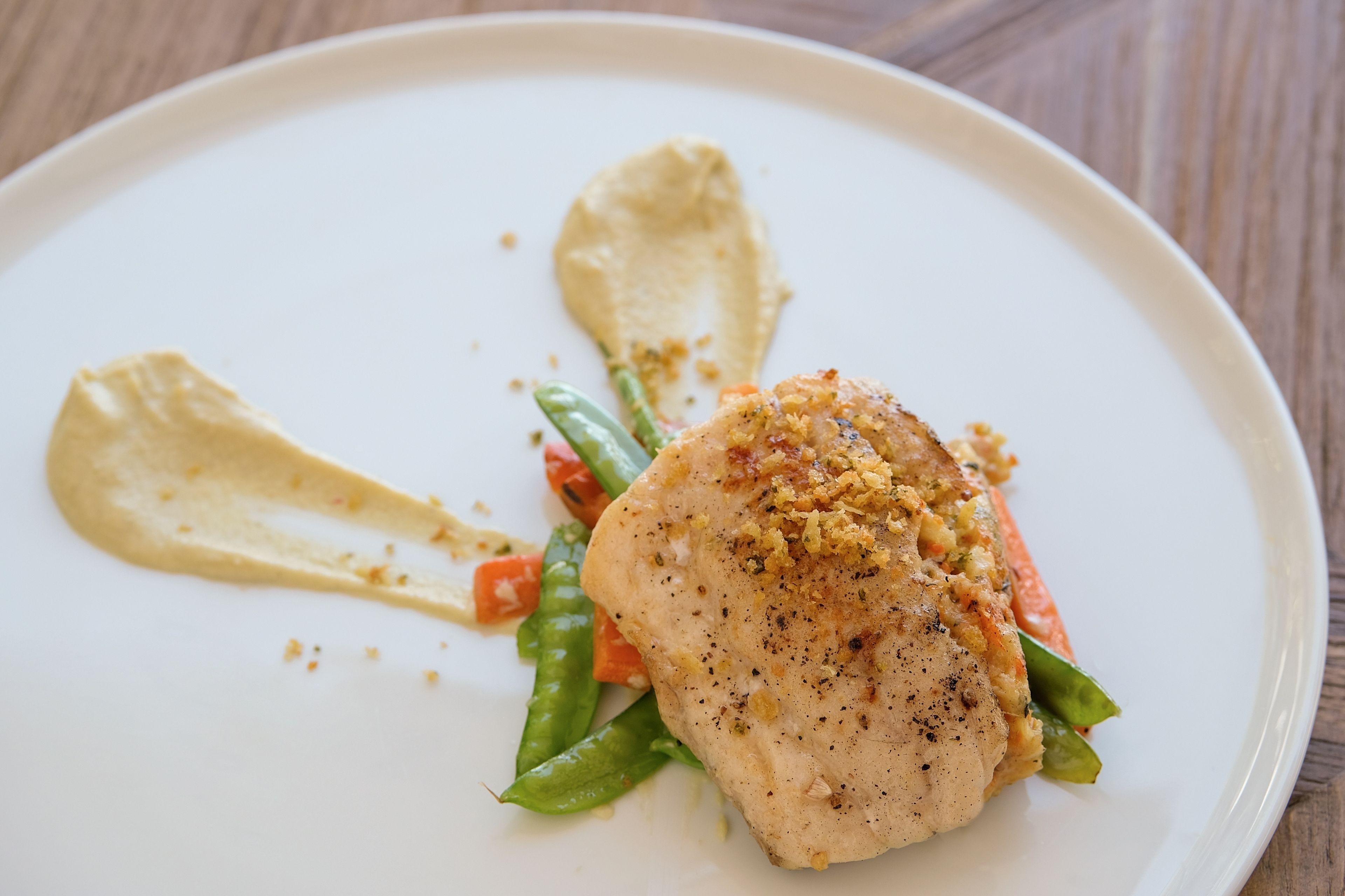 Une assiette blanche contenant un morceau de poulet, des haricots verts, des carottes et une cuillerée de sauce.