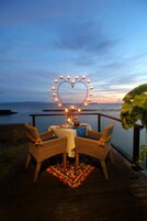 A romantic outdoor dining setup with wicker chairs, a table with a white tablecloth, and a heart-shaped light decoration.