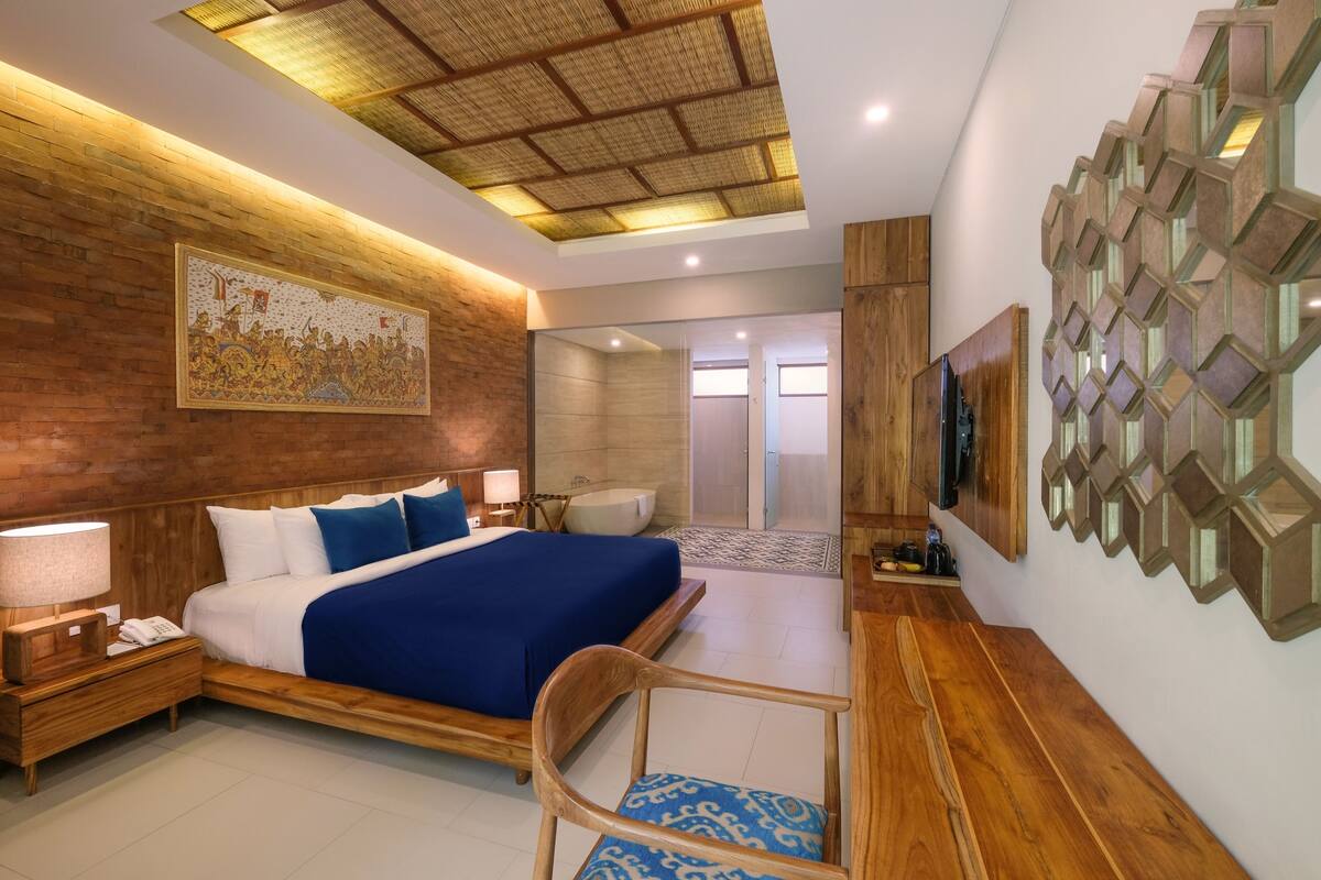 Una habitación de hotel moderna con una cama grande, cabecera de madera, un televisor montado en la pared y un techo con diseño geométrico.