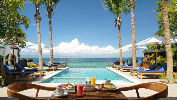 A poolside dining area with a table set for breakfast, overlooking a clear blue ocean. - Sagara Candidasa by AHM (Karangasem)