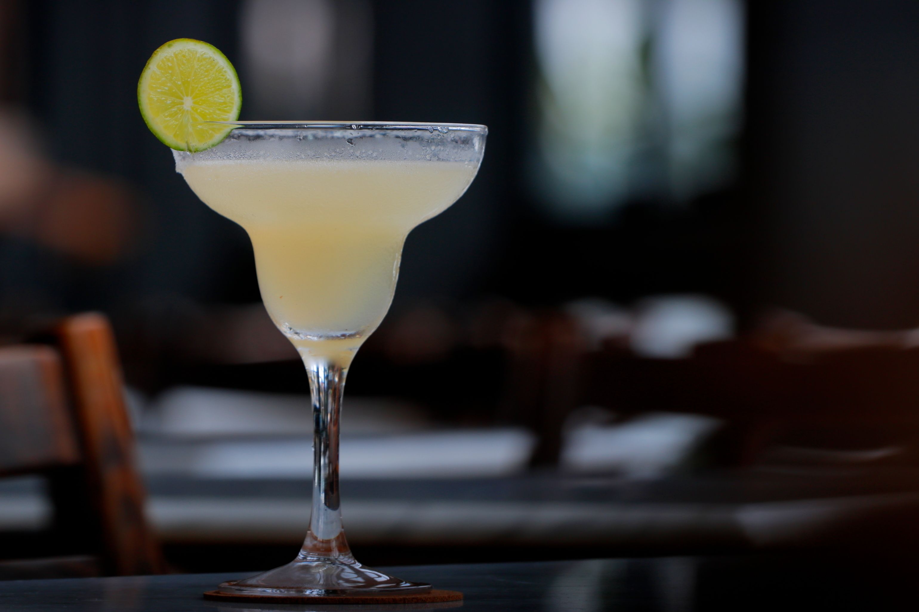 Een margarita in een longdrinkglas met een limoenpartje, geplaatst op een onderzetter.