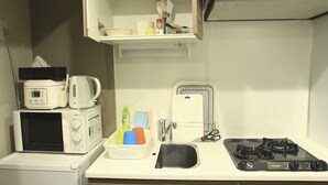A compact kitchen with a microwave, toaster, kettle, and a gas stove. - 2500 Comics Room (Tokyo)