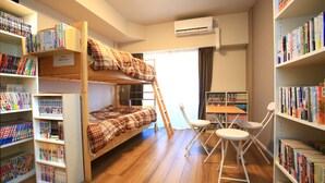 A bunk bed with a plaid blanket, wooden flooring, and bookshelves filled with books. - 2500 Comics Room (Tokyo)