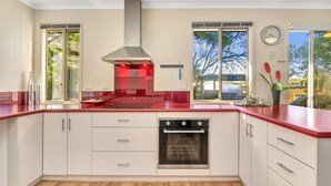 A modern kitchen with white cabinets, a red countertop, a stainless steel range hood, and an oven. - All Decked Out (Port Willunga)