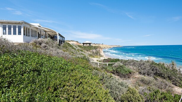 A coastal property with a white building, a beach, and ocean views. - All Decked Out (Port Willunga)