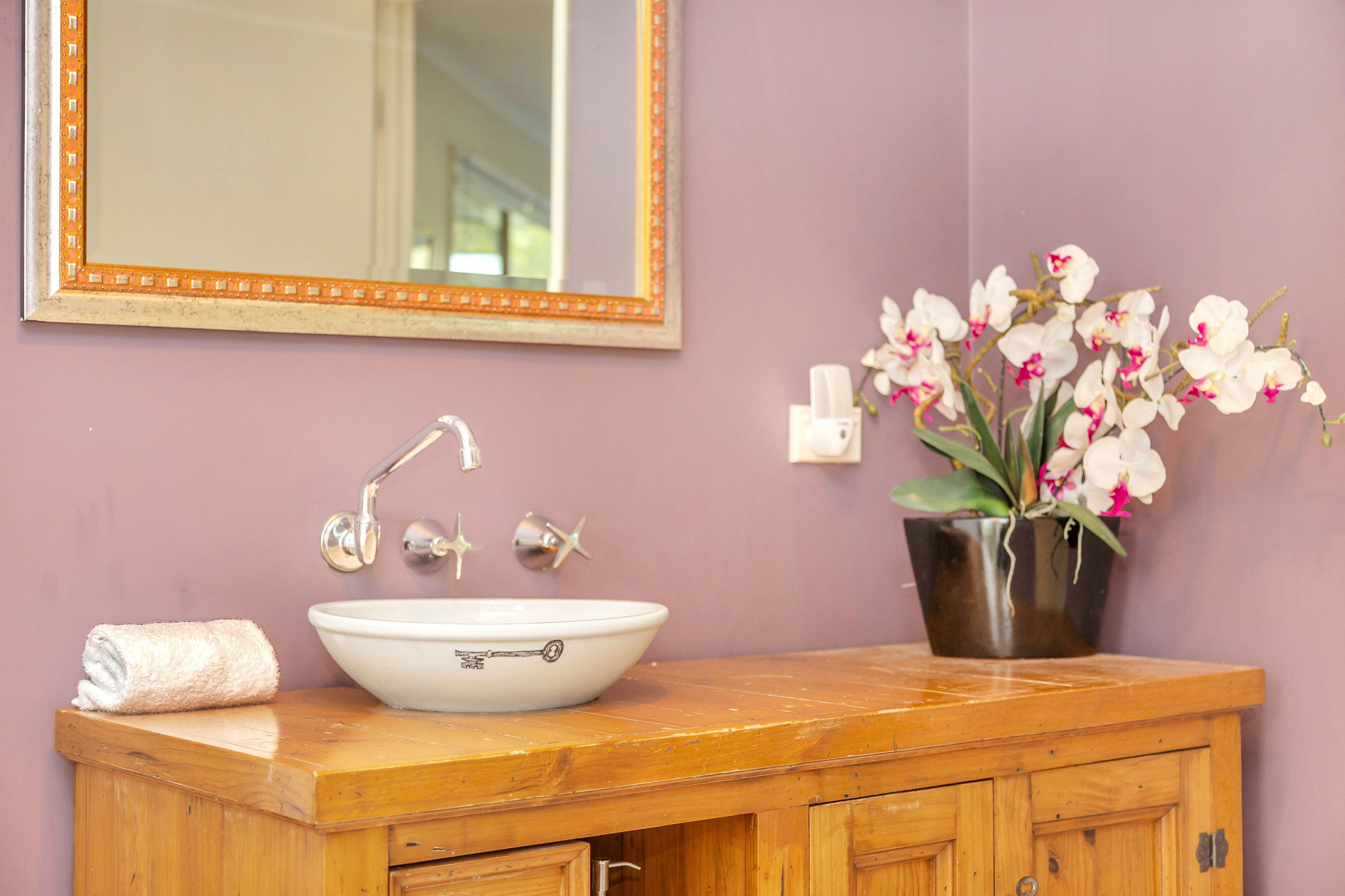 A bathroom with a white sink, a wooden vanity, a mirror with an orange frame, and a potted orchid plant.