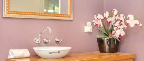 A bathroom with a white sink, a wooden vanity, a mirror with an orange frame, and a potted orchid plant.