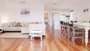 A modern living room with a white sofa, a coffee table, and a dining area with wooden chairs and a white table.