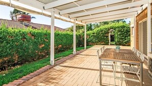 A covered patio area with a table and chairs, surrounded by a brick pathway and green hedges. - Moana Magic (Moana)