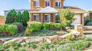 A two-story house with a brick facade, a tiled roof, and a front yard with shrubs and rocks. - Moana Magic (Moana)