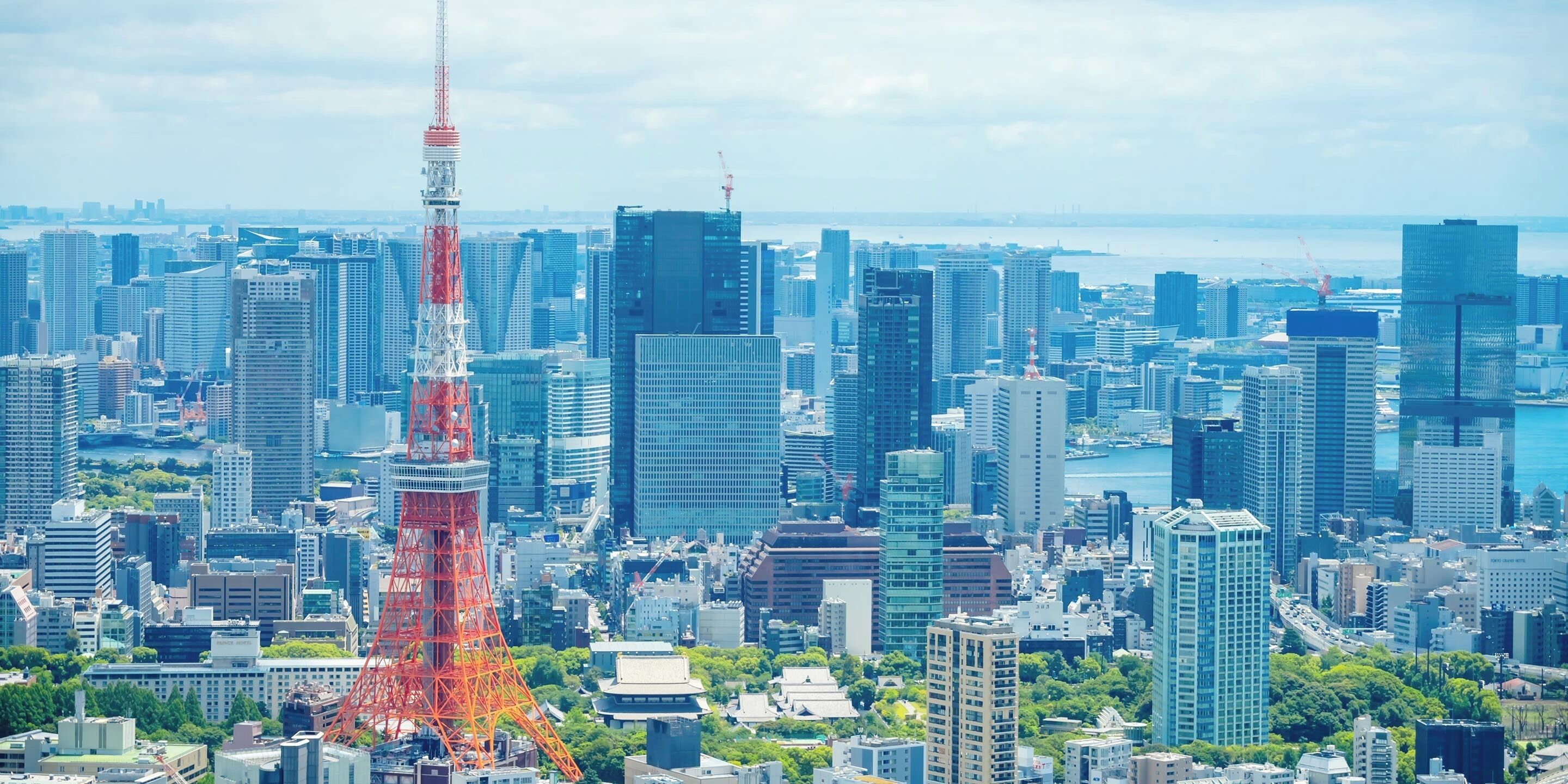 A cityscape with a prominent red tower, modern high-rise buildings, and a body of water in the background.